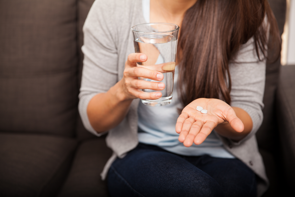 a woman holds a glass of water in one hand and pills in the other while listening to her doctor explain the benefits of suboxone