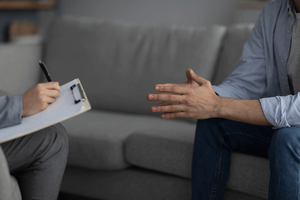 a patient holds his hands together while sitting on a couch with his therapist discussing medication-assisted treatment for opioid use disorder